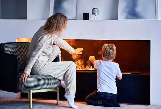 Woman sits near fireplace with little boy in living room.