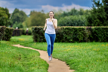 Fototapeta premium Happy woman in sportswear is running on path in park.