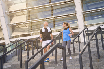 Active sportive mature couple, man and woman in sportswear walking down the stairs after exercising together outdoors