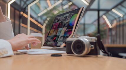 A photographer or retoucher works remotely with a laptop in a public space or coworking. A young woman in a white jacket works with images, a designer or a social media manager