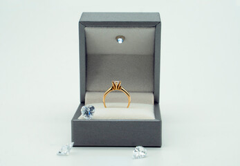 Gold ring in its box, surrounded by diamonds on white background.