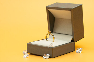 Shiny gold ring in its box on yellow background surrounded by diamonds