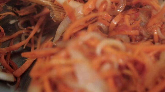 Wooden spoon stirring yam, carrots, tomato, and onion slices in pot
