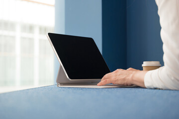 young freelance woman is sitting with a laptop in a public space and working on the Internet. Hands typing on the keyboard of a white thin laptop, close-up