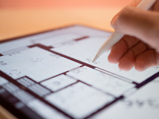 Interior Designer is working on a floor plan of building on mobile tablet computer. hand draws with...