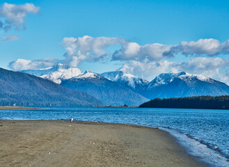 Alaskan beach with first snow on mountains and puffy clouds.