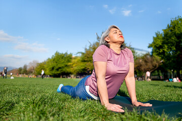 Mature woman doing yoga upward facing dog pose outdoor at an urban park