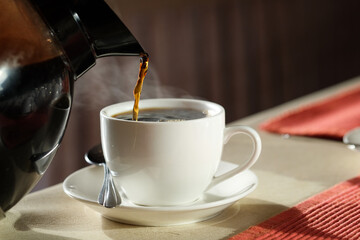 Morning of a new day,  hand of  young man pour black coffee in cup  and he drink coffee on the wooden table at home