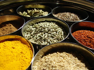 Indian spices in small containers, fennel, turmeric, cumin, cayenne, cardamom, close up