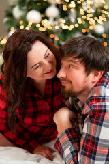 in love and happy man and woman in red checkered pajamas at the Christmas tree.