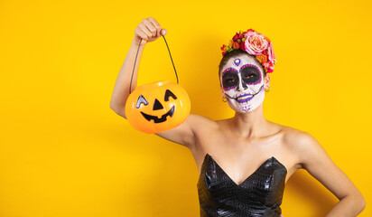 Mexican Catrina, portrait of young latin woman holding a plastic calaverita pumpkin for Halloween party in Mexico 