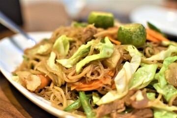 Hot stir fry noodles with vegetables, meat, seafood and calamansi in a white plate