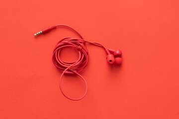 Red headphones with rolled wire, on a red background