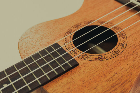 Close up of brown Ukulele on white background. Ukulele strings, saddle, soundhole, ukulele body, neck, fretboard.