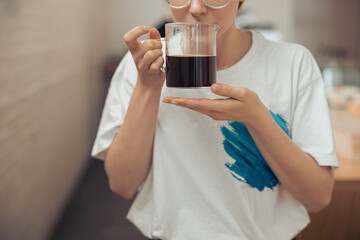 Young woman holding glass cup of aromatic coffee
