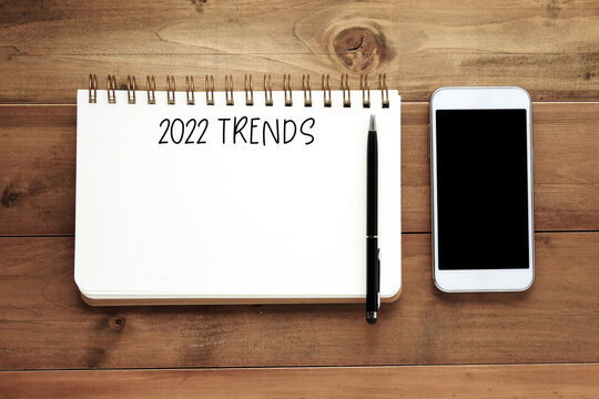 2022 trends on blank paper notebook , mobile phone and pen on wood background, new  year business trend mock up, template, copy space for text