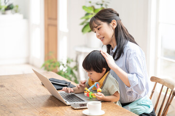 リモートで在宅ワークをする働きながら子供をなだめるママ　横からコ...