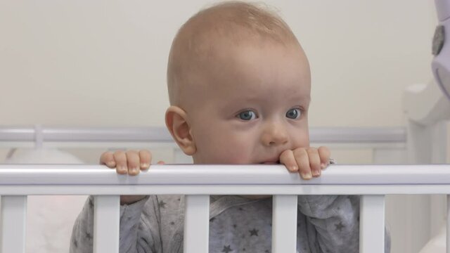 Baby sitting in infant bed, cute 7 months old baby boy playing in white rocking cradle at home. High quality 4k footage