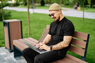 Fototapeta premium Stylish bearded millennial chatting working e-learning laptop at green park Distance education 