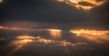 Blurred evening cloudscape. Dark autumnal clouds with gaps of sunlight beams breaking through the sky. No selective focus, defocused background.