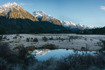 Snowy peak mountains reflected on small pond in Fiordland National Park, New Zealand.
