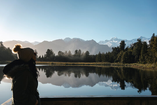 Woman looking at the mountains reflection of Lake Matheson, New Zealand