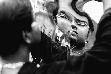 portrait of dark skinned Indian man looking into a distorted mirror