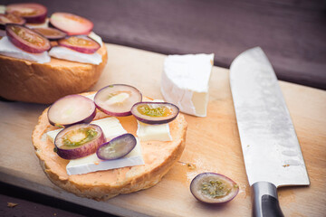 Delicious vegetarian food on a table. Large chef knife used to cut dark cherry tomatoes and brie cheese. Selective focus on the details, blurred background.