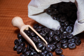 A linen bag with coffee beans and a wooden spoon on the background of natural wood texture, close up: making high-quality coffee in the morning, a morning drink for energy