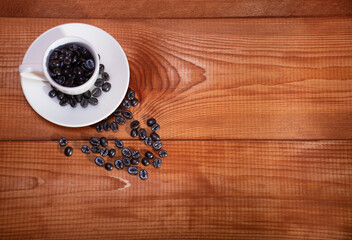White coffee cup is full of coffee beans on the texture of natural wood background: a place for text, a morning invigorating drink for coffee shops