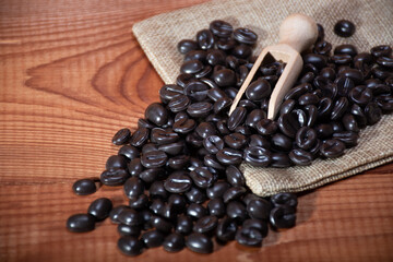 Empty linen bag on coffee beans and wooden spoon on the background of natural wood texture, close up: making high-quality coffee in the morning, a morning drink for energy, soft focus