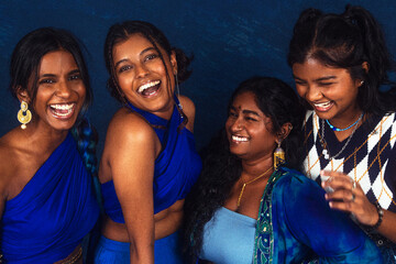 group portraits of dark skinned Indian women from Malaysia against a dark blue background, laughing