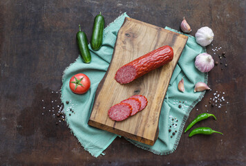 Sausage on wooden cutting board with vegetables, greens and spices. Food background. Top view.