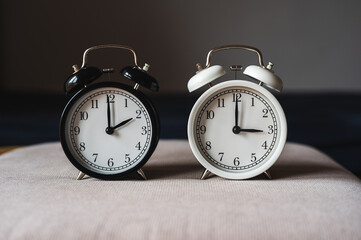 Two retro table clocks, black and white color, showing daylight saving time concept