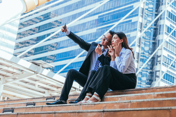 Business couple love sitting on stairs and selfie with cityscape background.