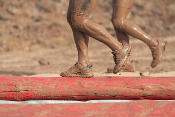 Mud race runners. Participants walking on the tree trunk, catches balance above the pit full of...