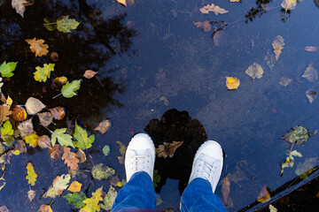 A person standing in a puddle in white rubber boots in autumn.