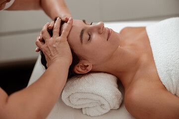 Fototapeta na wymiar Charming woman receiving professional scalp massage in spa salon
