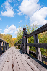A girl in black clothes stands with her back on a wooden bridge on an autumn sunny day