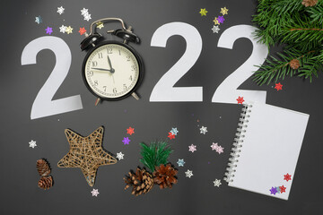 Layout on the theme of the New Year 2022 with numbers, clocks, toys and branches of a Christmas tree on a dark background.