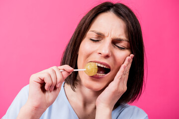 Young woman with sensitive teeth eating sweet lollipop on color background