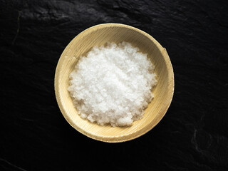 Coarse sea salt in bamboo bowl on slate worktop, background. Flat lay, top view.