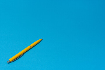 Perspective view of ballpoint pen on the blue background. Minimalist photo of yellow pen over blue...