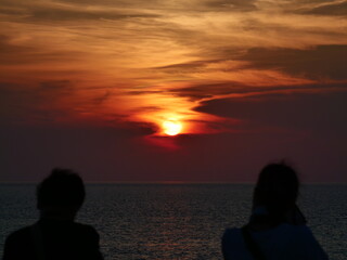 海に沈む夕日と夕焼けの空を見る2人の人影