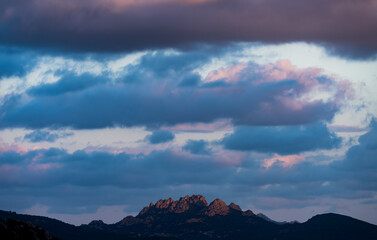 Stunning view of a dark, shadowy mountain range during a dramatic and cloudy sunrise. San Pantaleo, Sardinia, Italy.