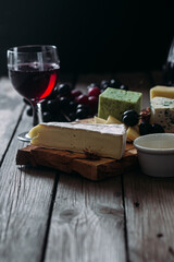 Cheese plate on a dark background. Brie, dor blue, gouda, grapes, nuts, wine