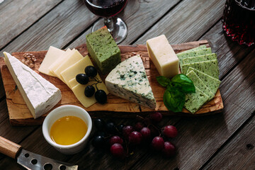 Cheese plate on a dark background. Brie, dor blue, gouda, grapes, nuts, wine