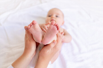 mom's hands hold the baby's legs in the crib on a white cotton bed, hygiene and care and care of the newborn
