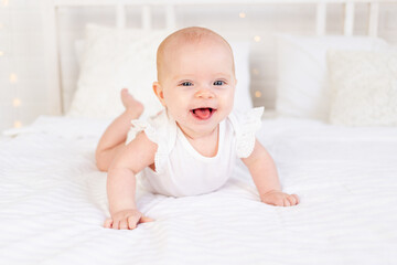 baby girl smiling or laughing lying on her stomach on a white cotton bed at home