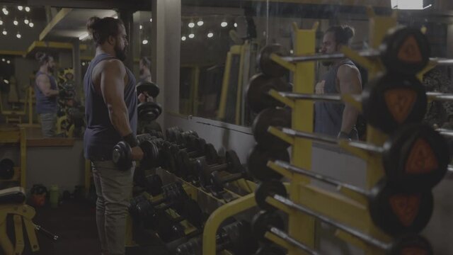 S-Log. professional athlete bodybuilder working out in the indoor gym. weight lifting and bodybuilding, muscle strengthening workout. man doing biceps exercise with heavy dumbbells. fitness video